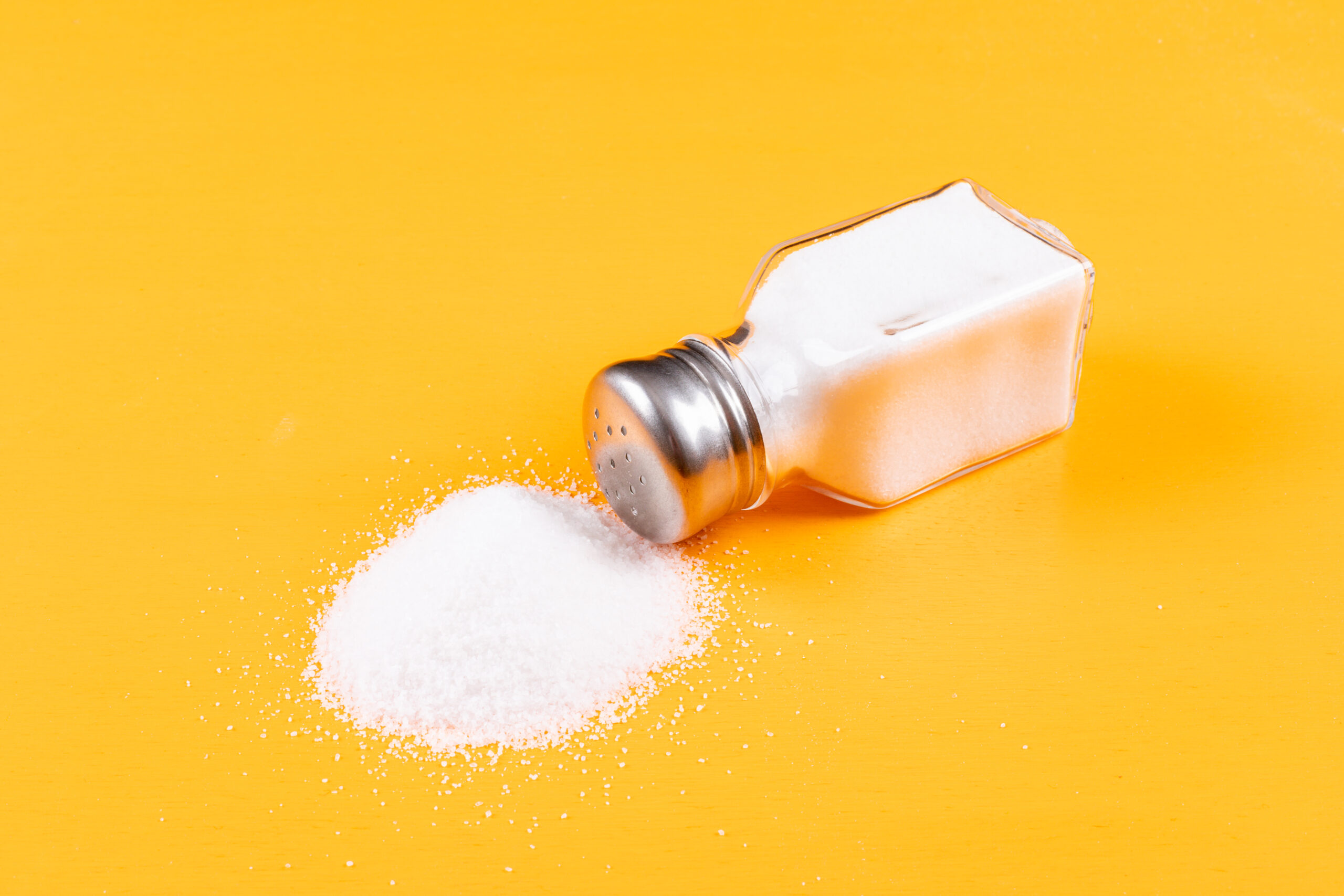 High angle view sea salt coming out of salt shaker on orange background. horizontal