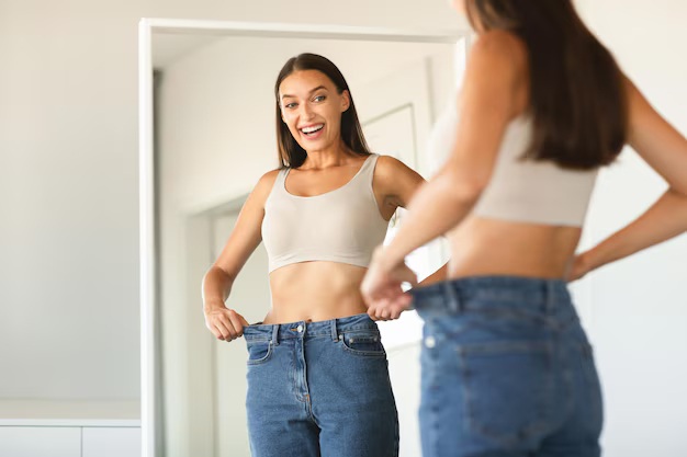 successful-slimming-concept-excited-caucasian-lady-wearing-jeans-after-weight-loss-comparing-size-posing-near-mirror_116547-42164