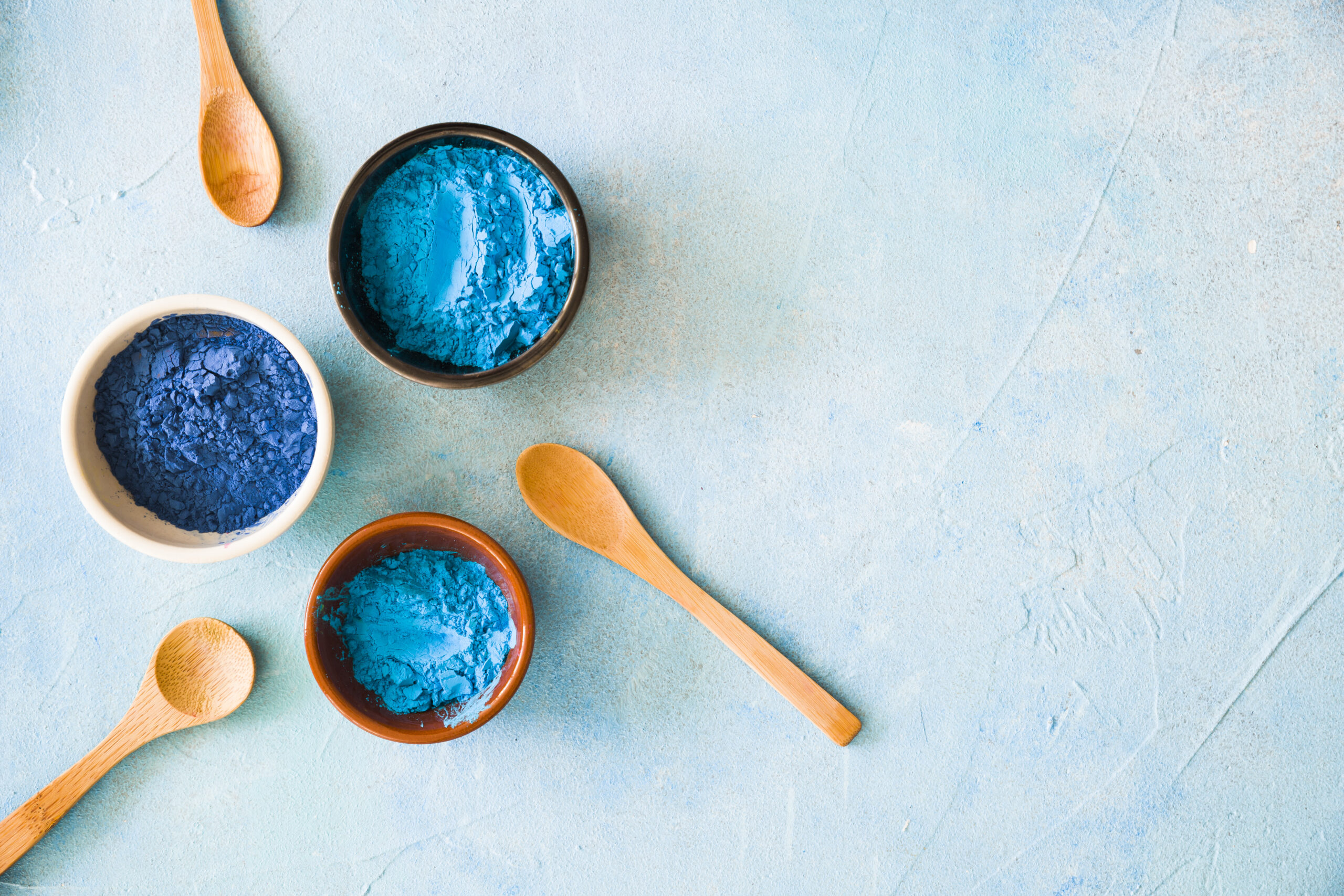 bowls-with-holi-color-powder-wooden-spoon-painted-background