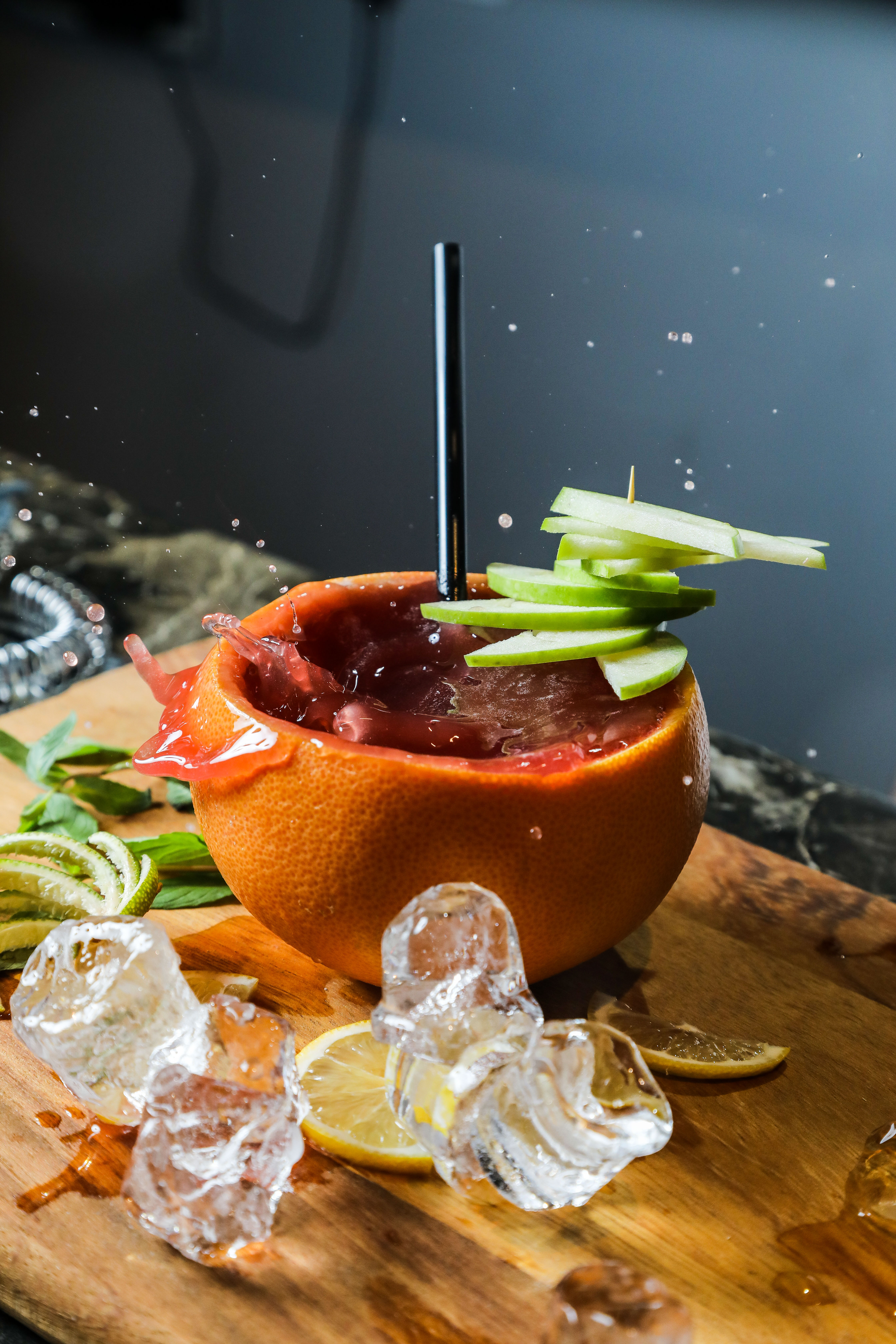 side view fruit cocktail in orange peel with apple and lemon wedges on a cutting board